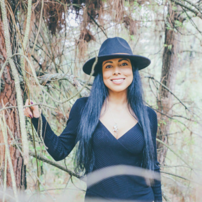 woman in black hat with long black hair smiles in fir trees
